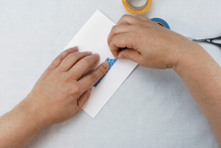 person pressing torn tape to a piece of white card stock